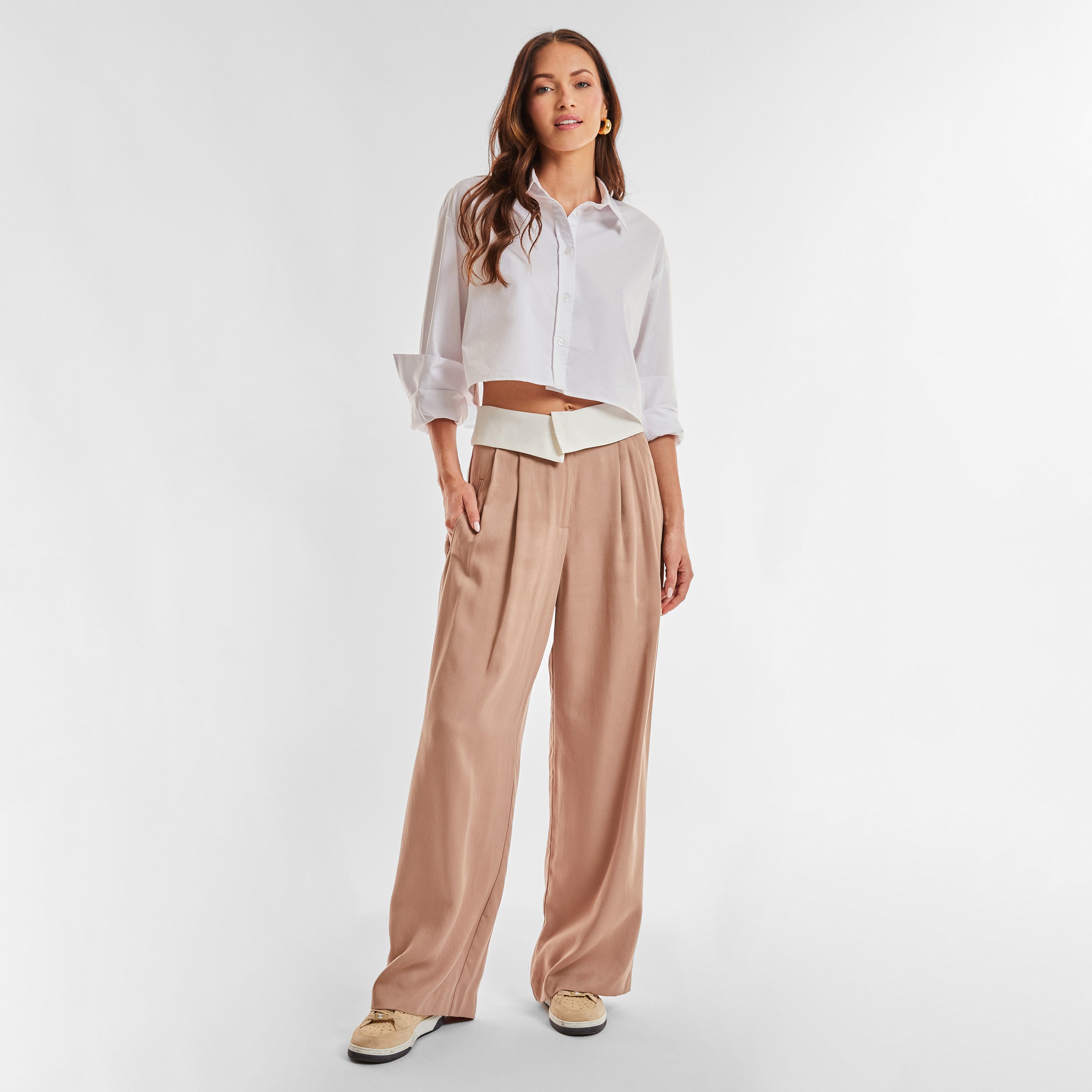 Full view of woman wearing light brown trousers with white foldover waistband detail.