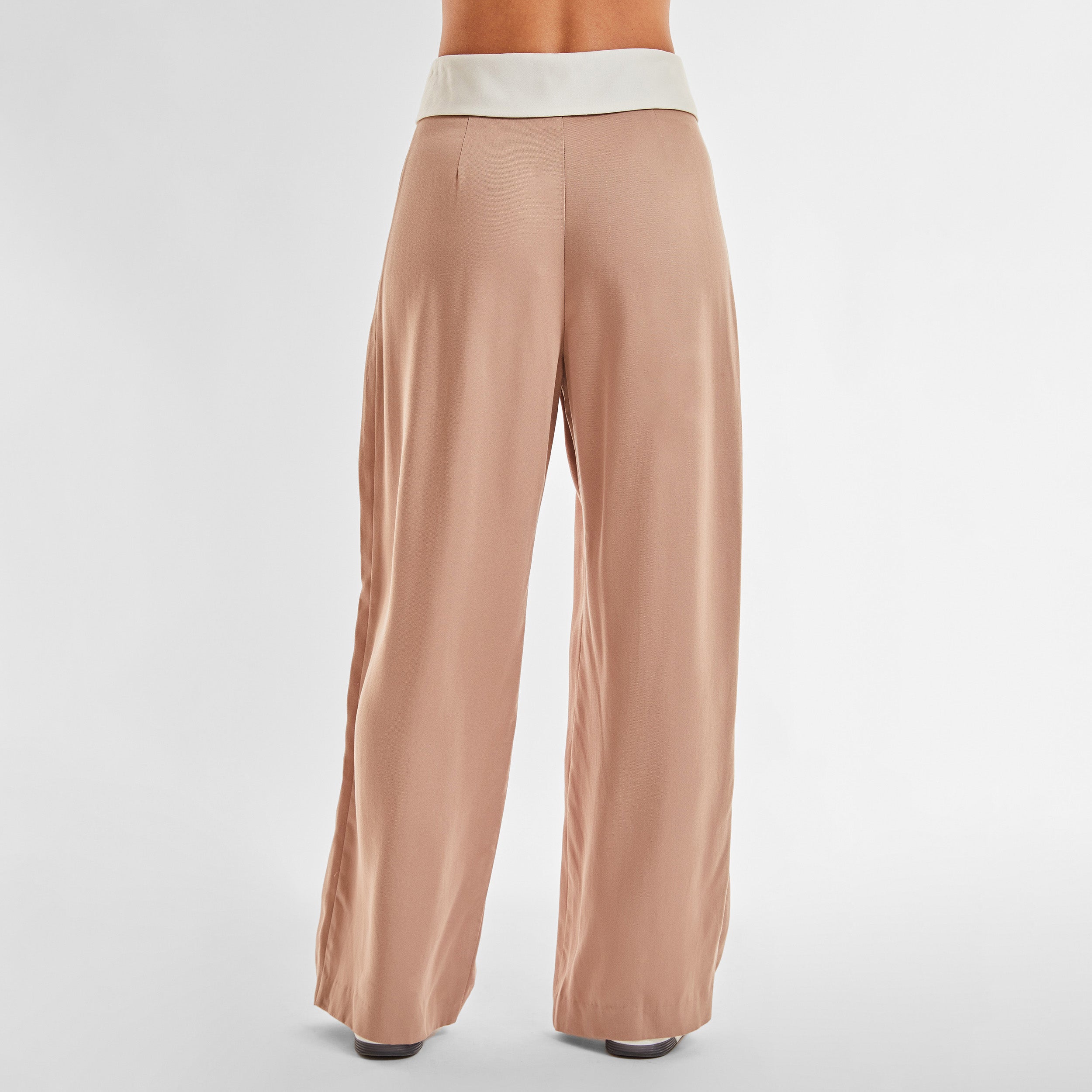 Rear view of woman wearing light brown trousers with white foldover waistband detail.