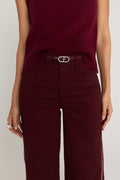 The Mabel Belt in merlot worn at the waist over the Aria Coated Flare Jean in Merlot, showing the silver oval buckle