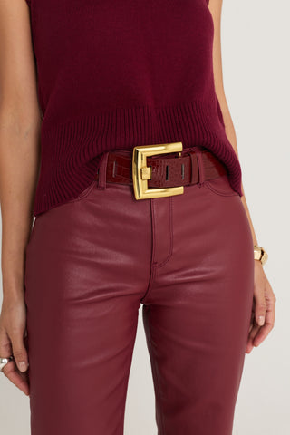 The Loire Belt in merlot worn at the waist over the Aria Coated Flare Jean in Merlot, showing the oversized gold buckle