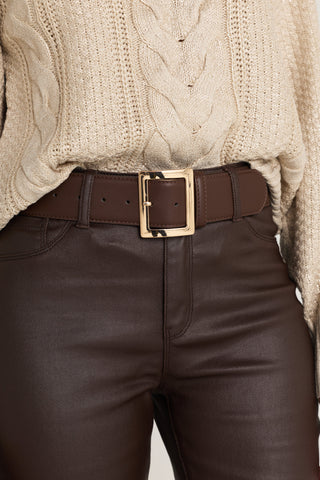 The Josie Belt in Espresso worn at the waist over the Aria Coated Flare Jean in Espresso, showing the wide strap and square gold buckle