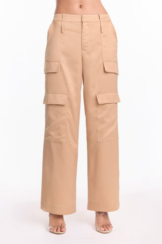 A person wears the Milan Satin Cargo Pant - Gold (Preorder)—high-waisted, wide-leg cargo pants with multiple pockets—standing barefoot against a white background.