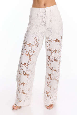 Wearing the Celeste Crochet Jean - White (Preorder), featuring high-waisted, wide-leg lace with large floral patterns, creates a flattering silhouette as the sheer fabric elegantly reveals skin underneath.