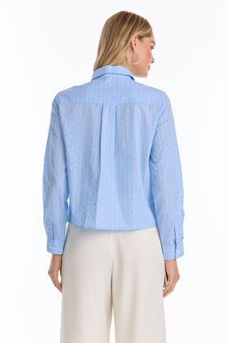 A woman with long blonde hair is seen from the back wearing the Josefina Crystal Button Up - Blue Stripe (Preorder) and white wide-leg pants against a plain white background.