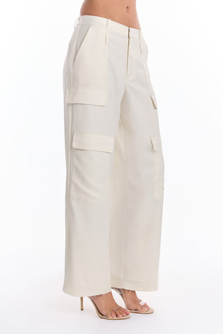 Someone wearing the Milan Satin Cargo Pant in Pearl, featuring high-waisted, wide-leg cargo styling with large side pockets, paired with beige high-heeled sandals, shown waist down against a white background.