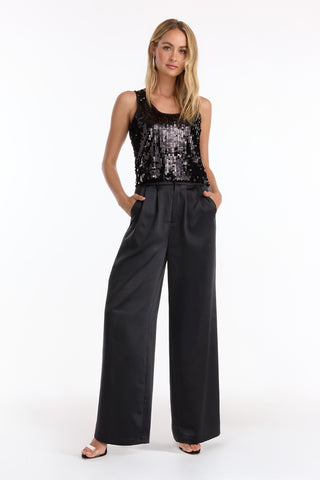 A woman stands with hands in pockets, wearing the Sophia Sequin Tank - Black (Preorder), wide-leg black trousers, and open-toe heels against a plain white background.