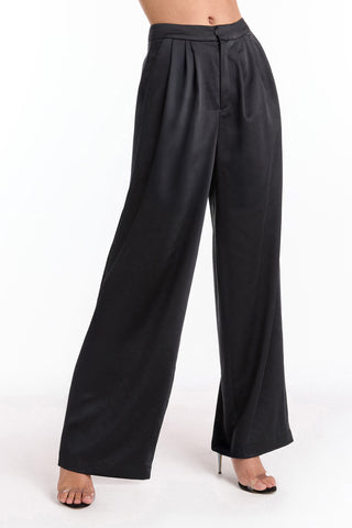 Wearing the Valentina Satin Pant - Black with a high waist and wide-leg fit, the person stands in high-heeled sandals against a white background. The upper body remains out of view.