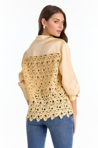A woman in the Amelia Silky Lace Blouse - Butter Yellow (Preorder), featuring a relaxed fit, sheer lace back, and long sleeves, stands facing away while looking over her shoulder, paired with blue jeans.