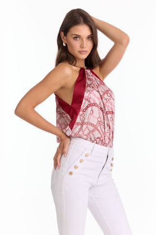 A woman poses confidently in the Mika Silky Halter Top - Pink Chain (Preorder) and white high-waisted pants with gold buttons, creating a standout summer look.