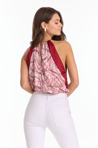 A woman faces away from the camera in the Mika Silky Halter Top - Pink Chain (Preorder), styled with high-waisted white pants, loose hair, and large round earrings—a standout summer look.