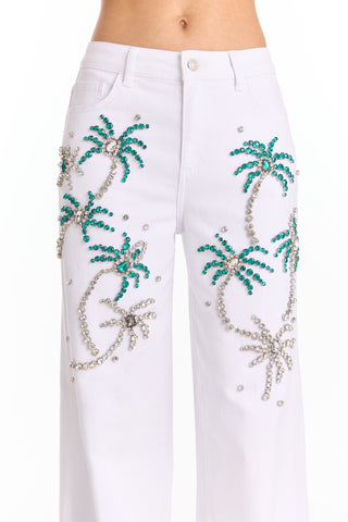 A close-up of the Crystal Palm High Rise Jean - White, showcasing a tropical palm tree pattern with green and silver jeweled accents and rhinestones on soft, 4-way stretch denim.