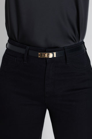 The Nicola Belt in black and gold worn at the waist, showing the slim strap and gold rectangular buckle