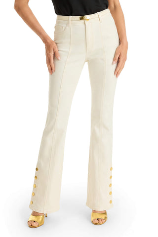 A person wearing Veronica Button Jean - Ivory mid-rise flares with gold buttons on the outer legs, paired with a black top and yellow heeled sandals, stands with hands resting on their thighs.