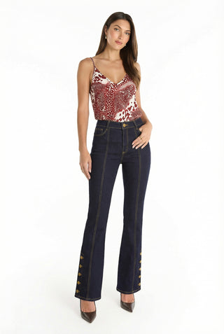 A woman stands against a white background wearing the Veronica Button Jean - Indigo, featuring mid-rise flares in dark blue four-way stretch denim with gold buttons at the lower legs for a leg-elongating silhouette.