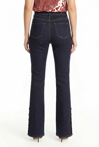 Someone stands with their back to the camera wearing the Veronica Button Jean - Indigo, a dark blue, four-way stretch denim with visible back pockets and button details at the mid-rise flare hem, paired with a red and white sleeveless top.