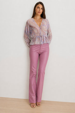 A woman stands against a light background, wearing the Whitney Chiffon Top in pastel paisley—a feminine statement blouse with long sheer sleeves—paired with light purple high-waisted pants. She has long brown hair and is wearing open-toed heels.