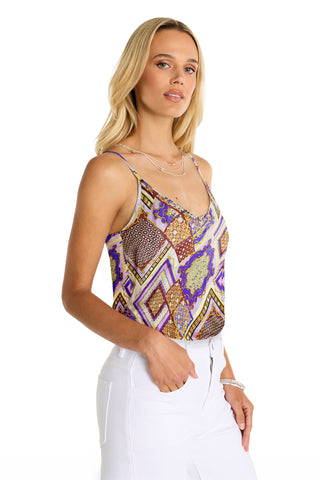 A woman with long blonde hair wears the Yara Silk Camisole - Riviera Chain and white pants, posing with one hand in her pocket against a plain white background.