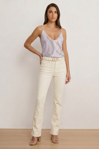 A woman with long brown hair and a neutral expression models the Yara Silk Camisole in pastel paisley against a plain background, styled with cream high-waisted belted pants and clear heeled sandals—ideal for effortless summer looks.