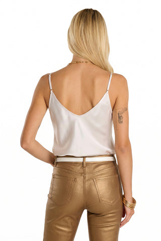 A woman with long blonde hair is seen from the back in a Yara Silk Camisole - Pearl and metallic gold pants, showing a left arm tattoo and accessorizing with gold bracelets and a necklace.