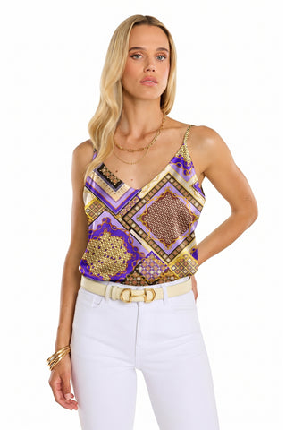 A woman with long blonde hair wears a gold chain necklace, gold bracelets, white pants with a white belt, and the Yara Silk Camisole - Riviera Chain, standing against a white background.